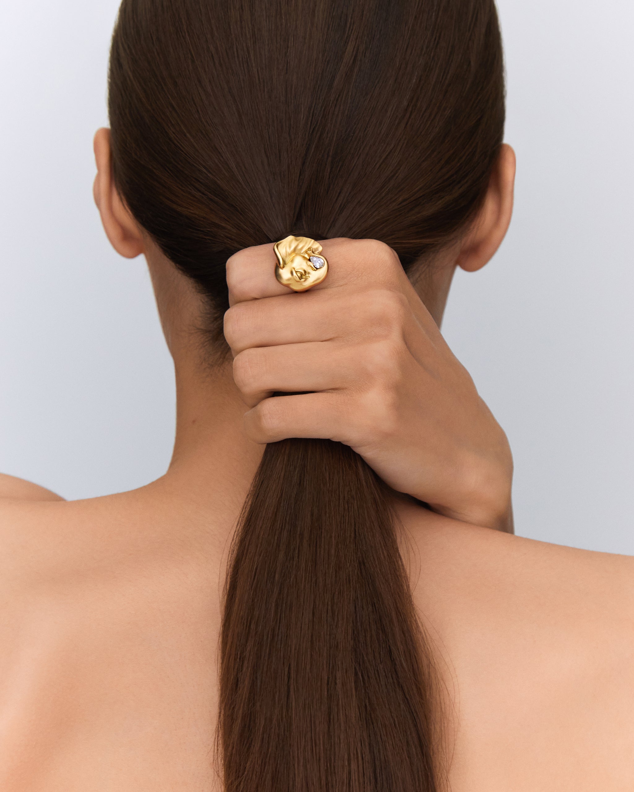 Femme de dos tenant ses cheveux, portant une bague en or recyclé avec un motif d'éléphant.